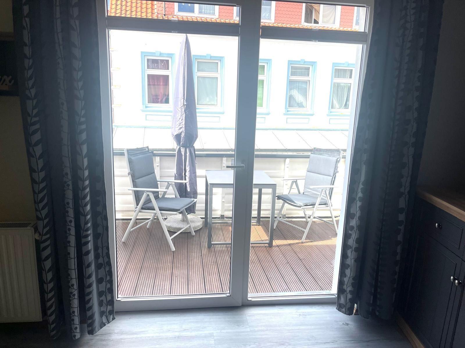 Terrasse mit Tisch und zwei Stühlen, Blick auf ein Gebäude mit blauen Fensterrahmen.