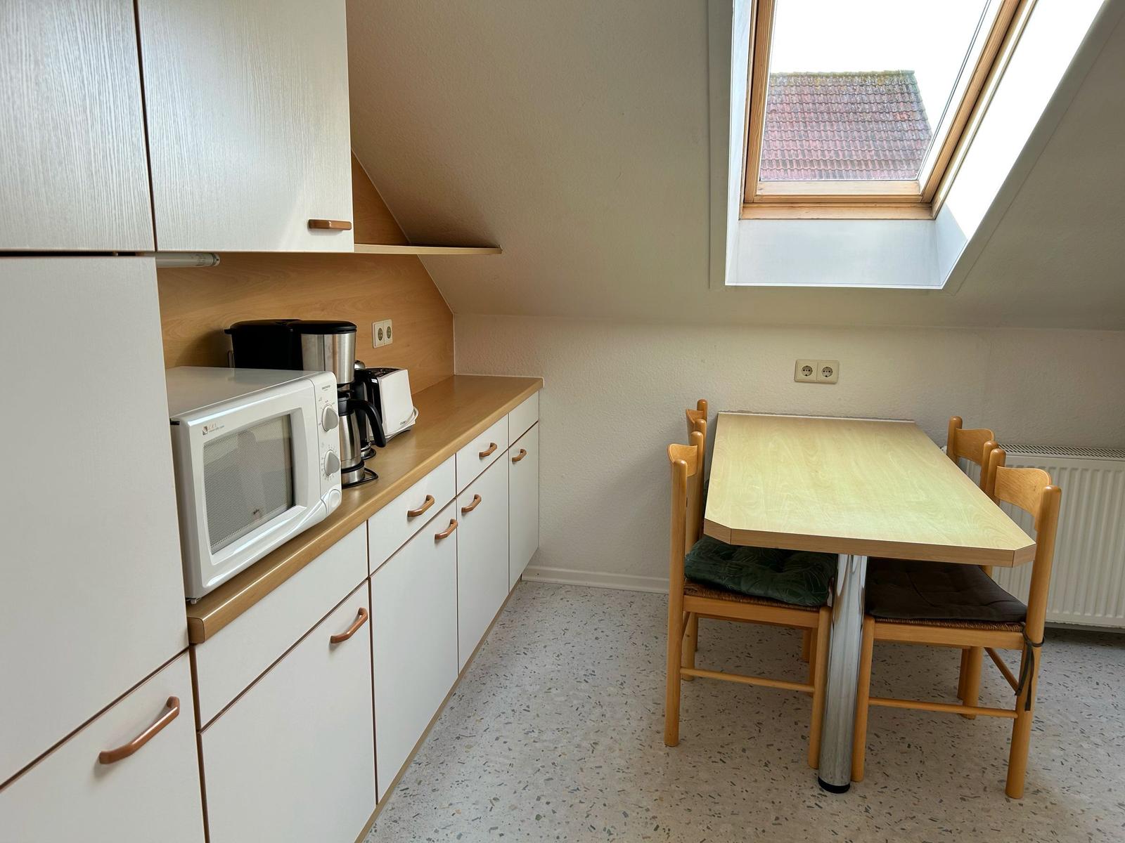 Küche mit Esstisch, Mikrowelle und Dachfenster.