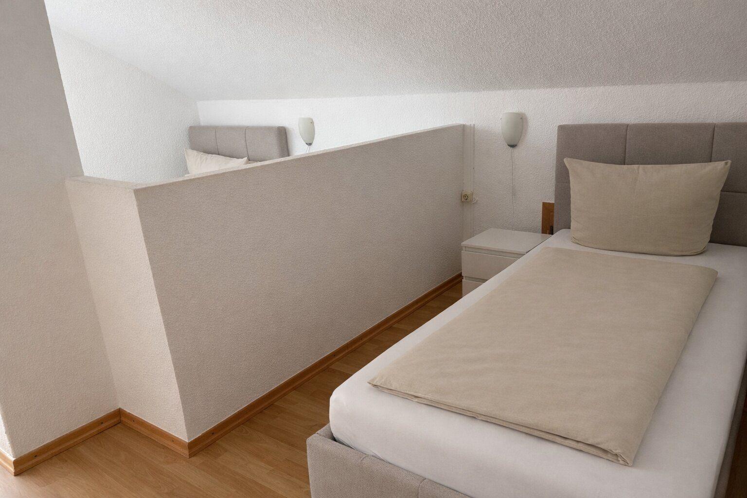 Zimmer mit zwei Einzelbetten und Holzboden. Wand trennt Schlafbereiche.