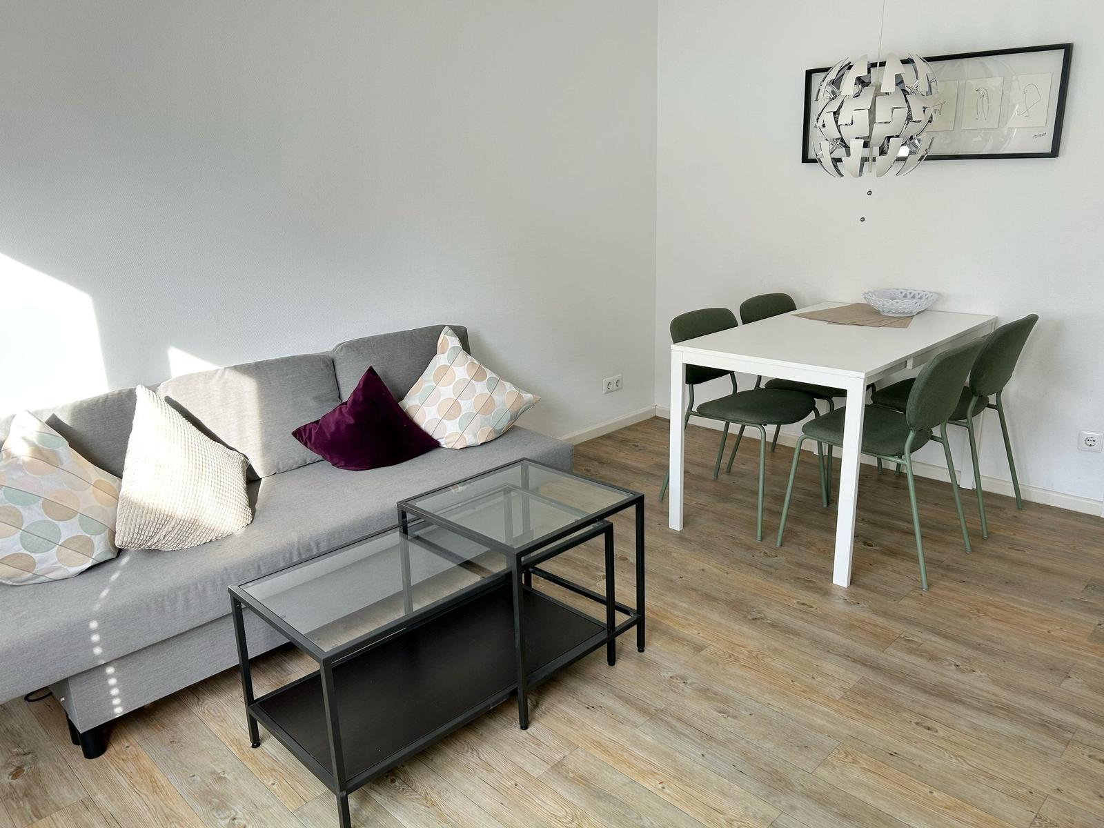 Wohn- und Essbereich mit Sofa, Tisch und Stühlen auf Holzboden.