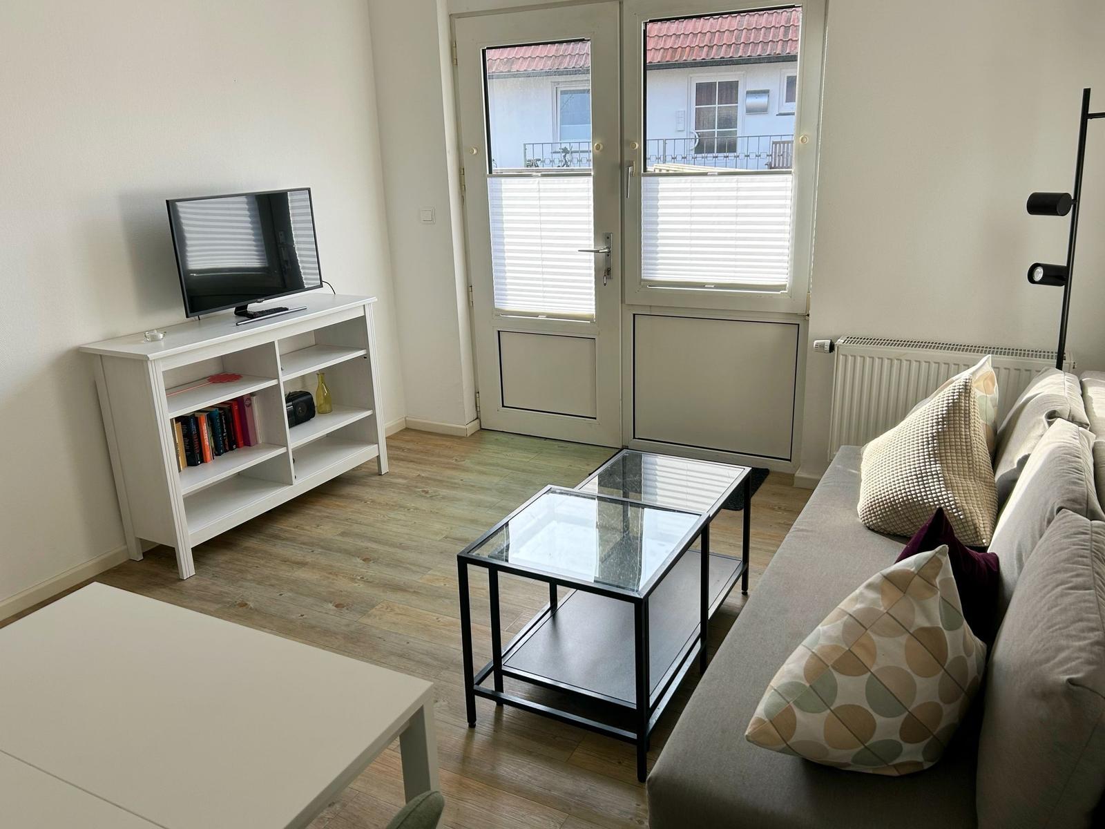 Wohnzimmer mit Sofa, Glas-Tisch und Fernseher auf weißem Sideboard.