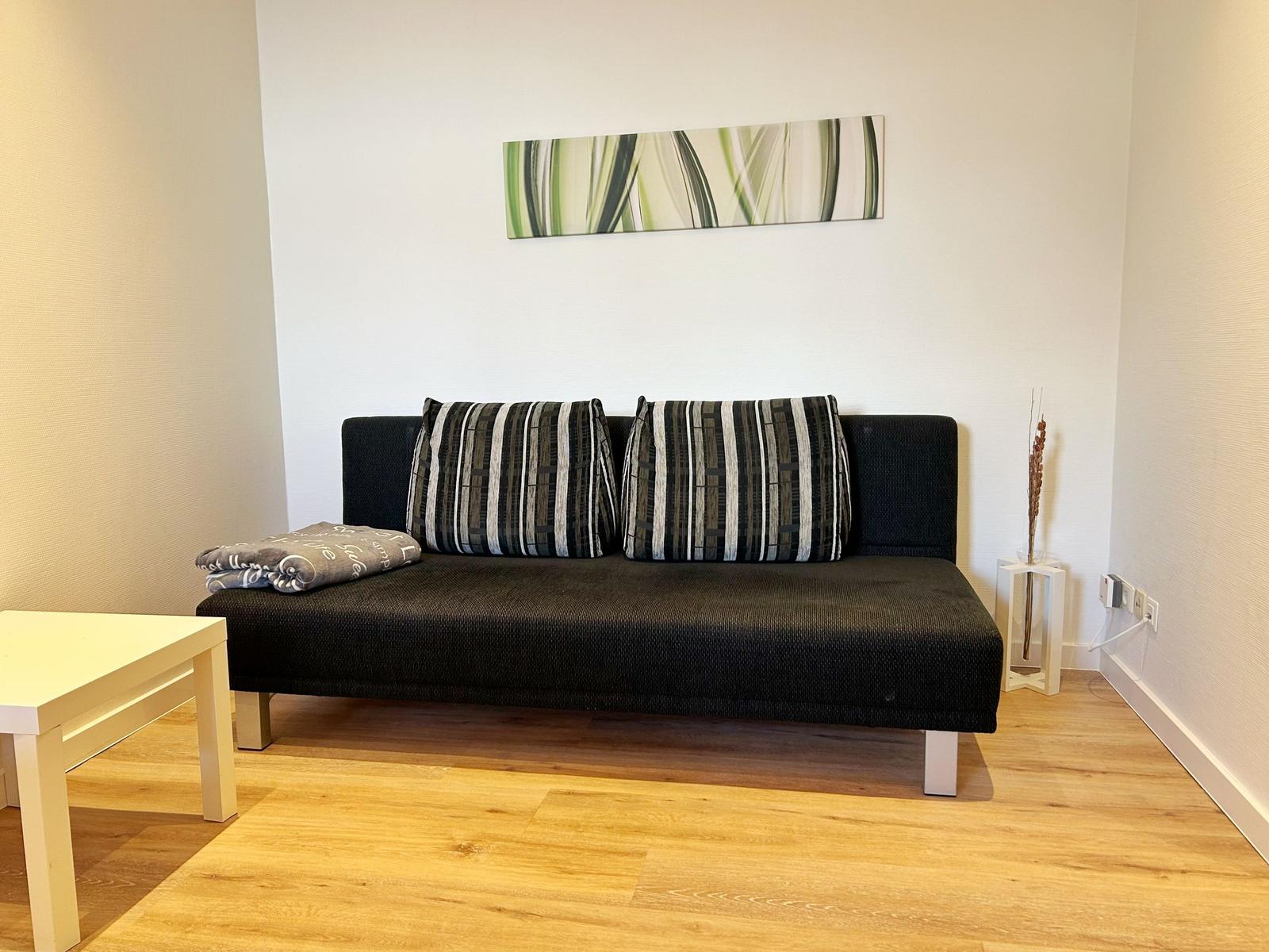 Schwarzes Sofa mit Kissen und Decke, Wandbild und Holzboden