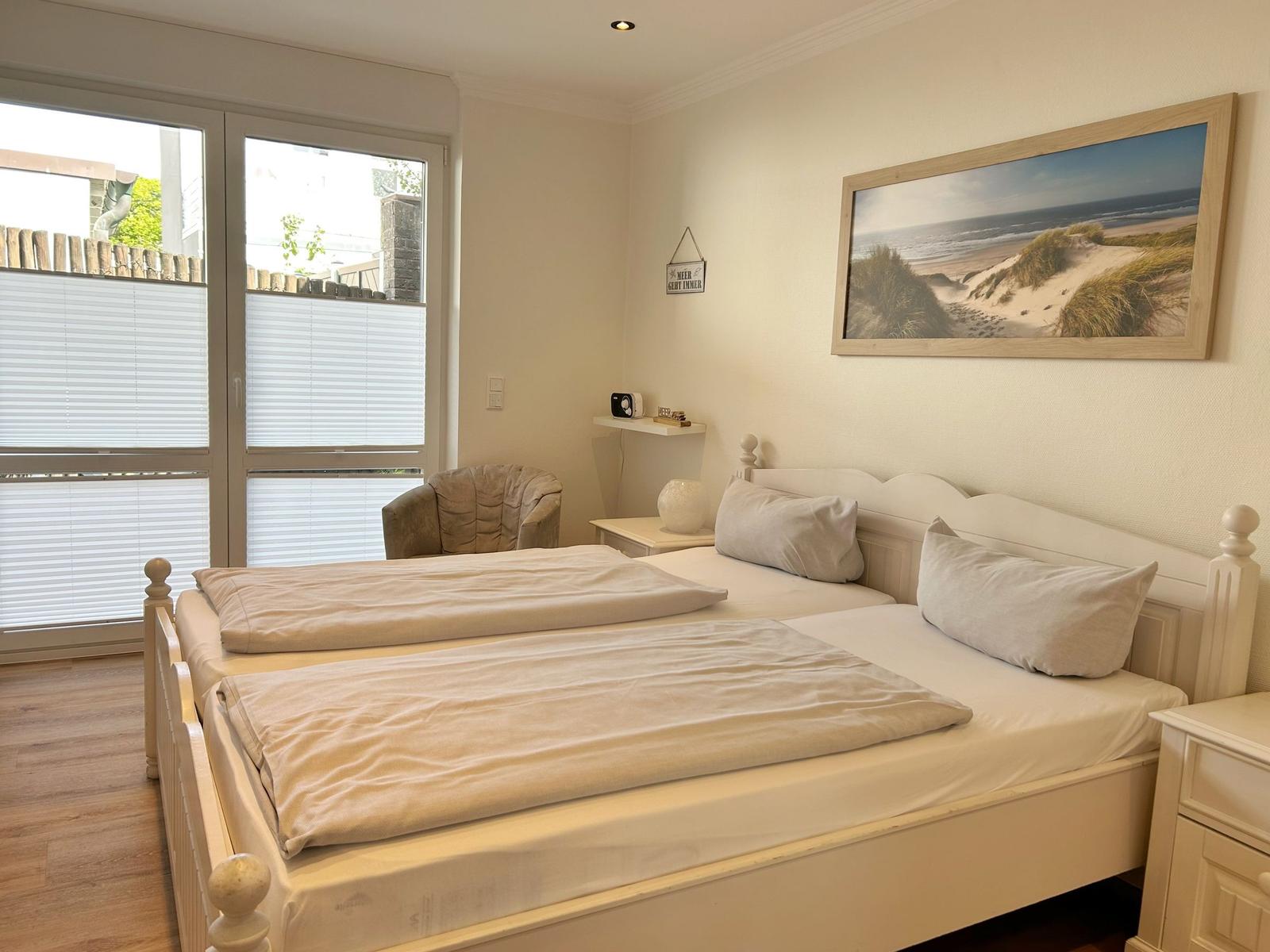 Schlafzimmer mit Doppelbett, Fenster und Strandbild an der Wand.
