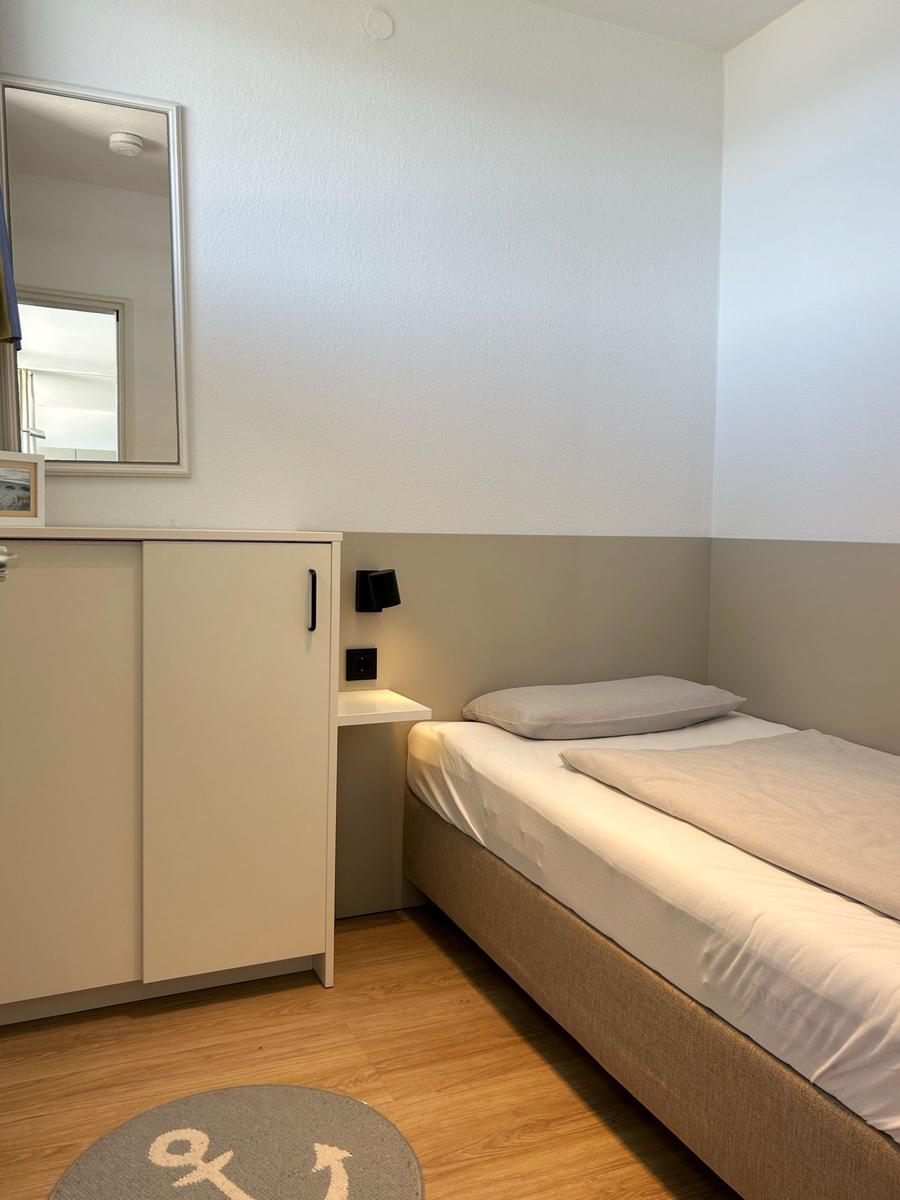 Schlafzimmer mit Einzelbett, Schrank und Spiegel an der Wand.