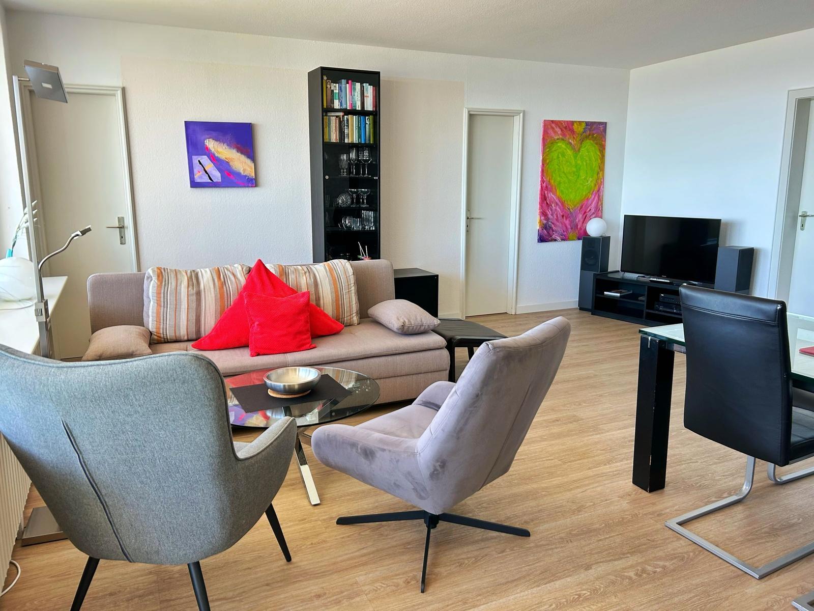 Wohnzimmer mit Sofa, zwei Sesseln, Fernseher und Gemälden an den Wänden.
