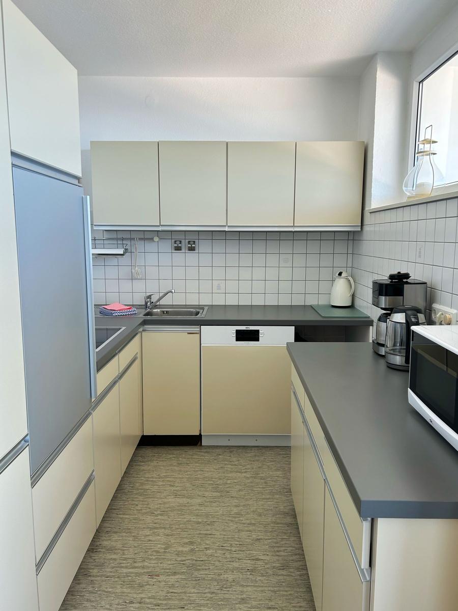 Küche mit hellen Schränken, Spüle, Kühlschrank und Mikrowelle.