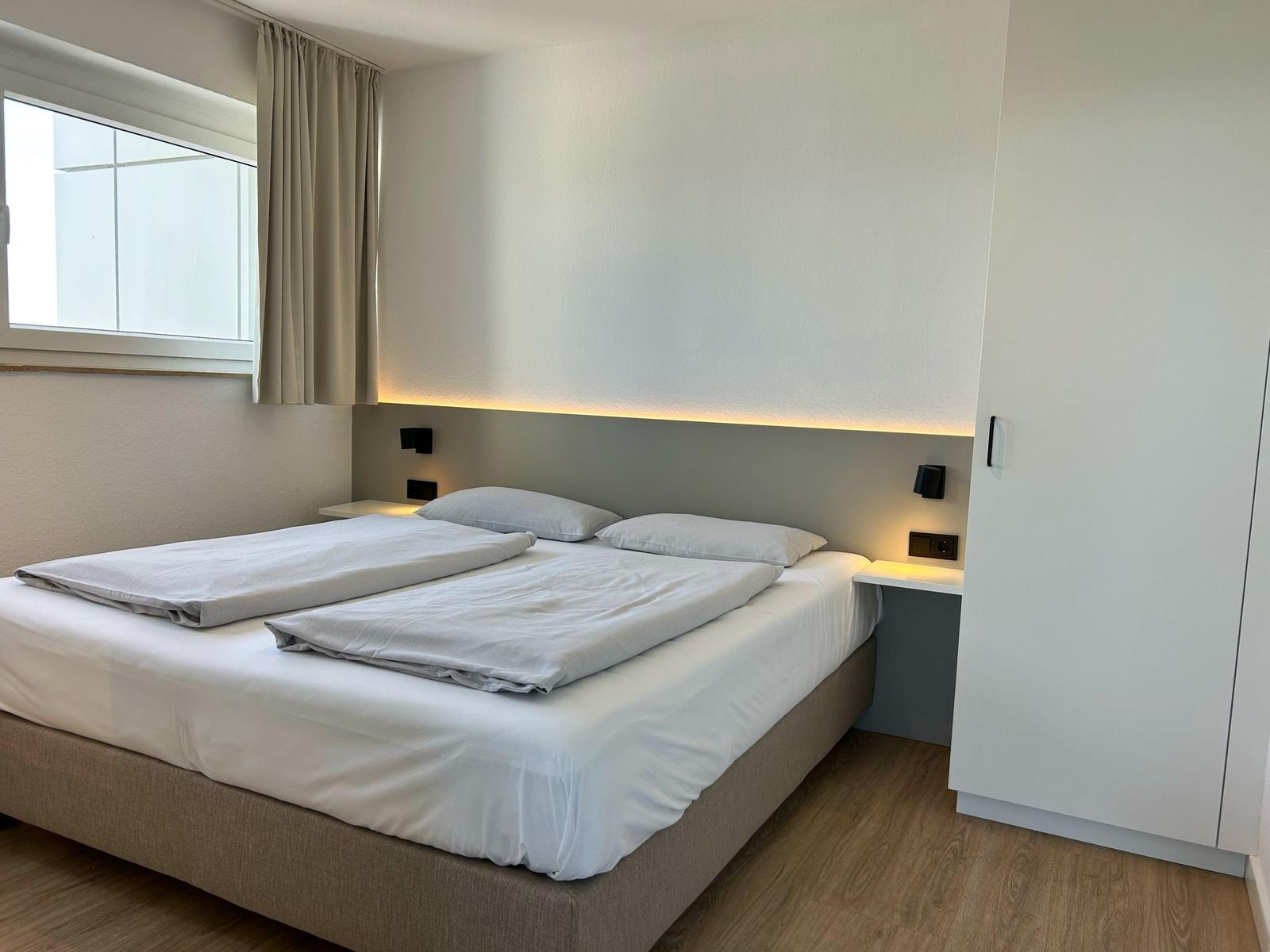 Schlafzimmer mit Doppelbett, Nachttischen und Fenster mit Vorhängen.