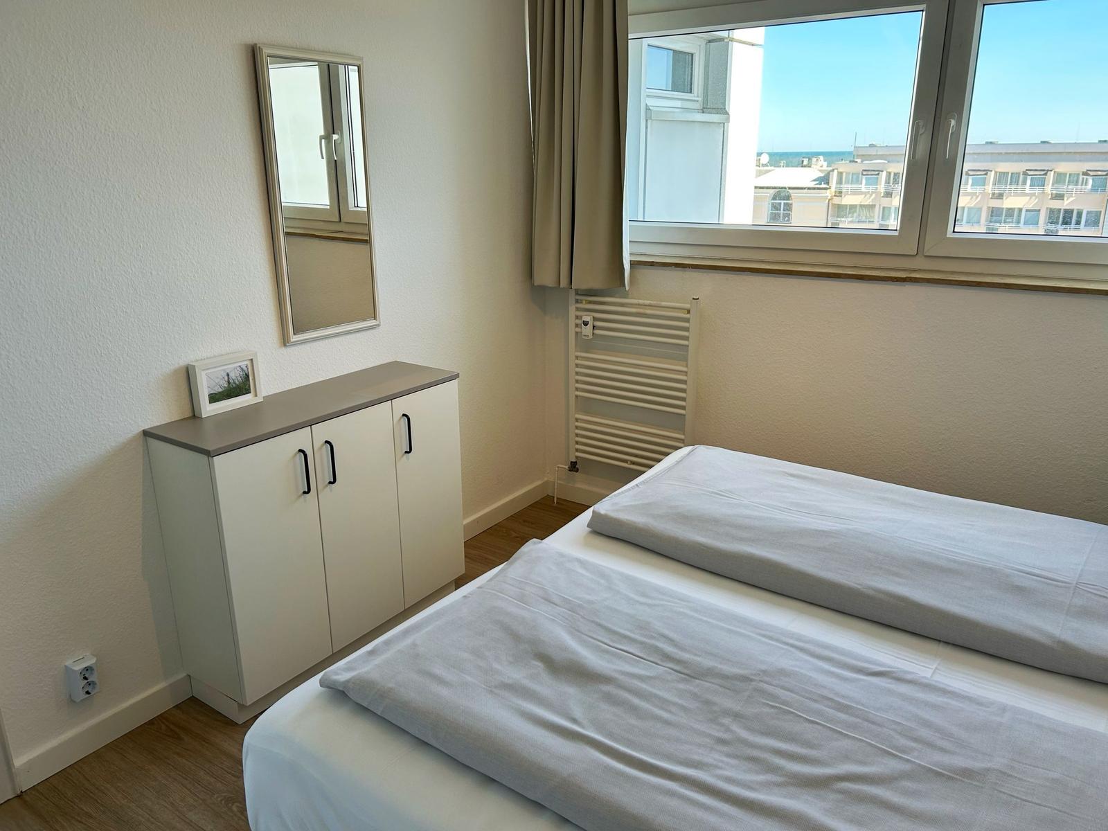 Schlafzimmer mit Bett, Kleiderschrank und Fensterblick auf Gebäude.