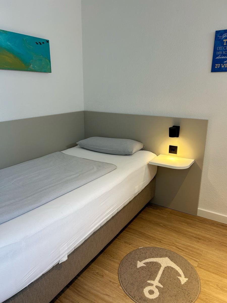 Ein Schlafzimmer mit einem Bett, einer Nachttischlampe und einem runden Teppich mit Ankermotiv.