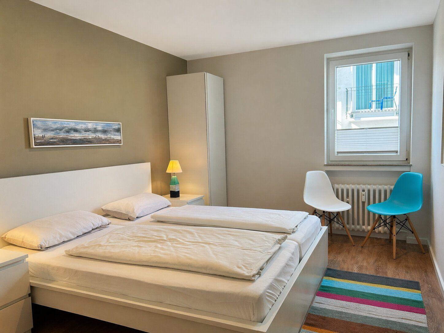 Schlafzimmer mit Doppelbett, zwei Stühlen und Fenster.