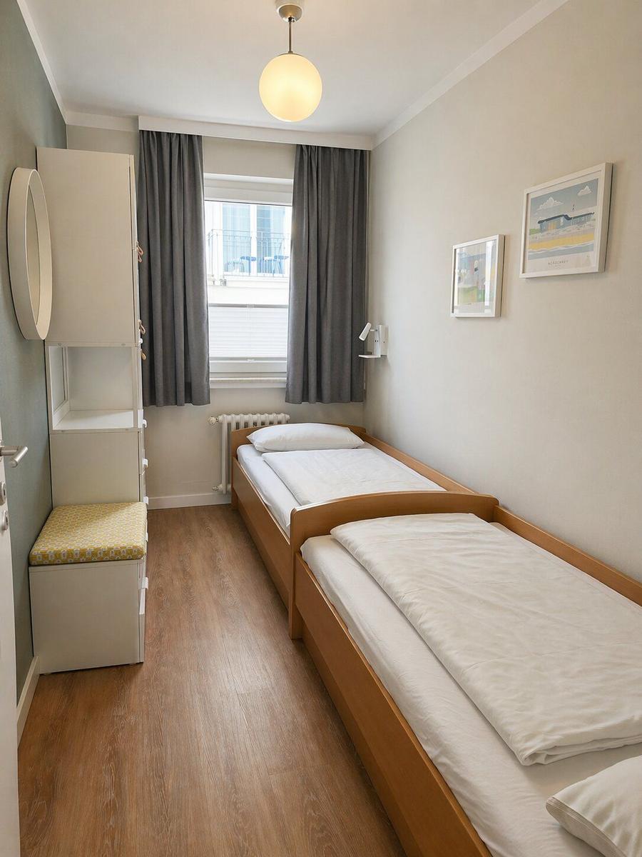 Zimmer mit zwei Einzelbetten, Fenster, Gardinen und Holzboden.