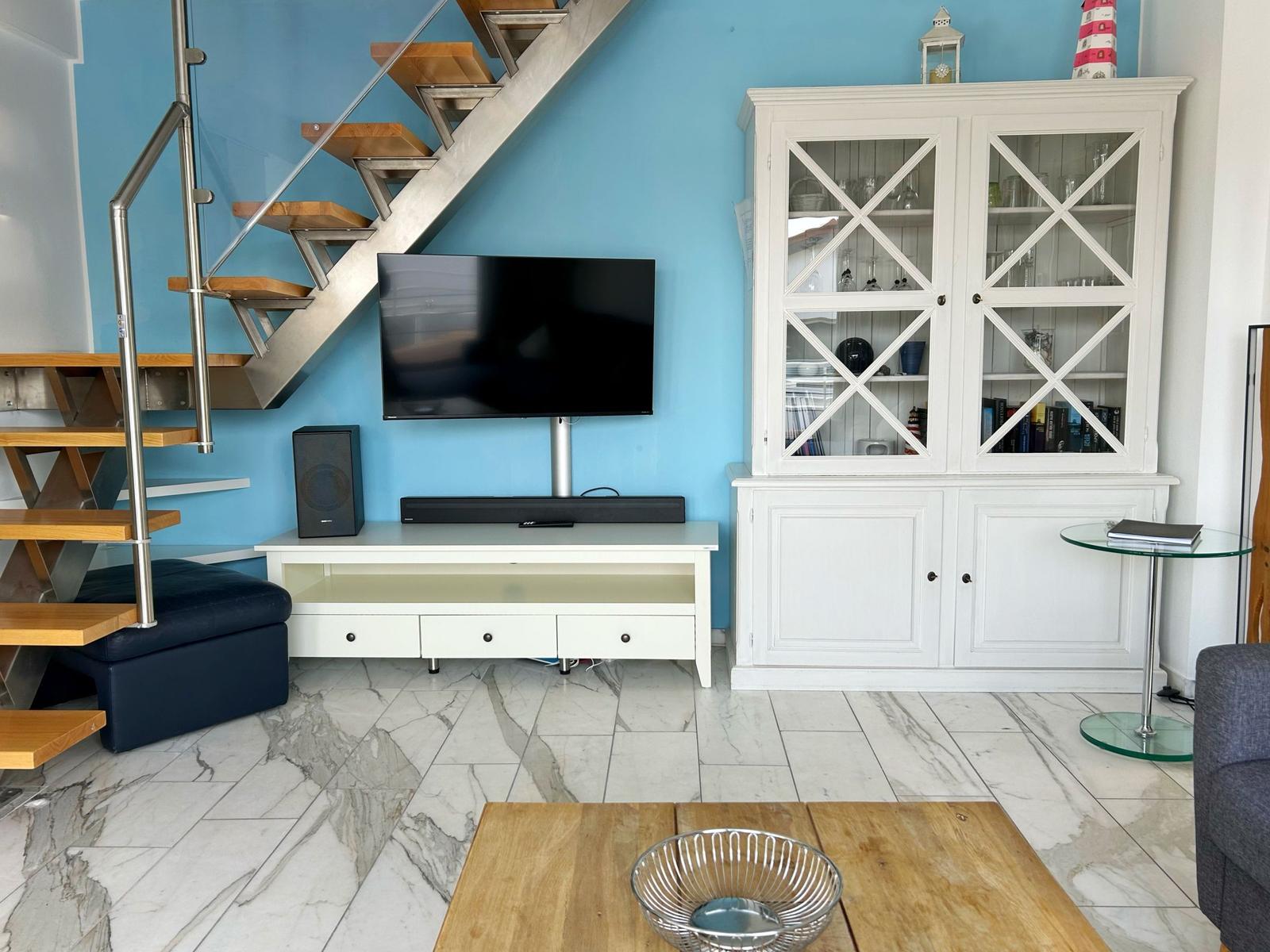 Wohnzimmer mit TV, Glaswand-Schrank und maritimer Dekoration.