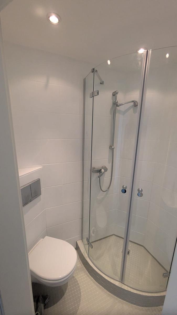Dusche mit Glaswand, Toilette und weißer Fliesenverkleidung