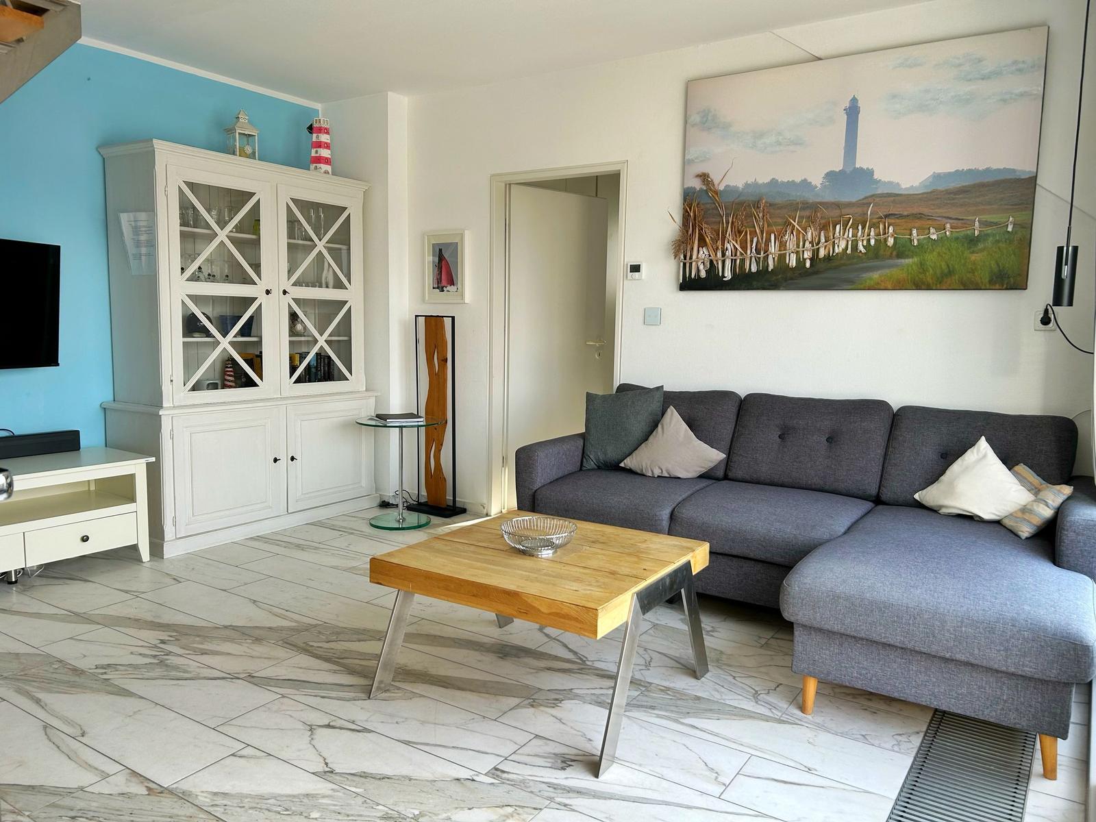 Wohnzimmer mit grauem Sofa, Holztablett und Wandbild mit Leuchtturm.