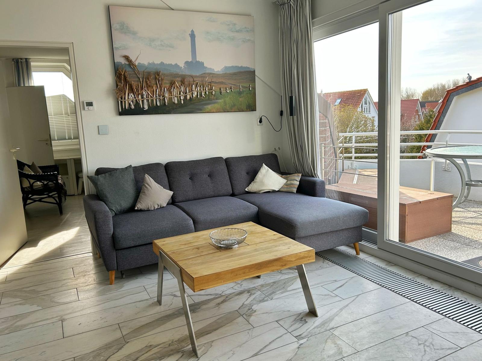 Wohnzimmer mit grauem Sofa, Holztisch und Blick auf Balkon.