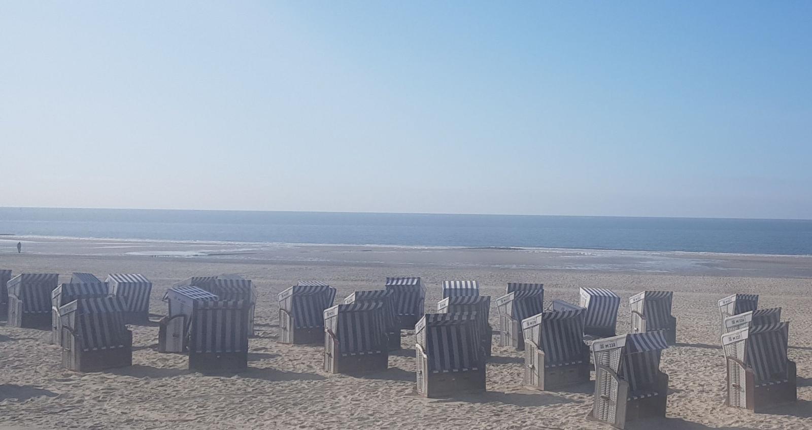 Strand mit Strandkörben und Meer im Hintergrund.