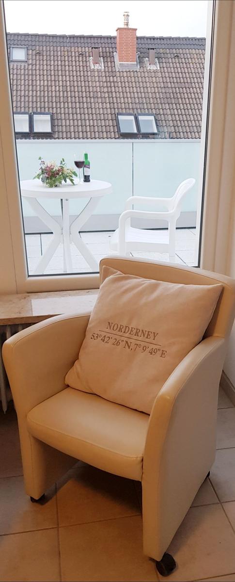 Beige Sitzsack mit Kissen vor Fenster zum Balkon mit Tisch und Stuhl.