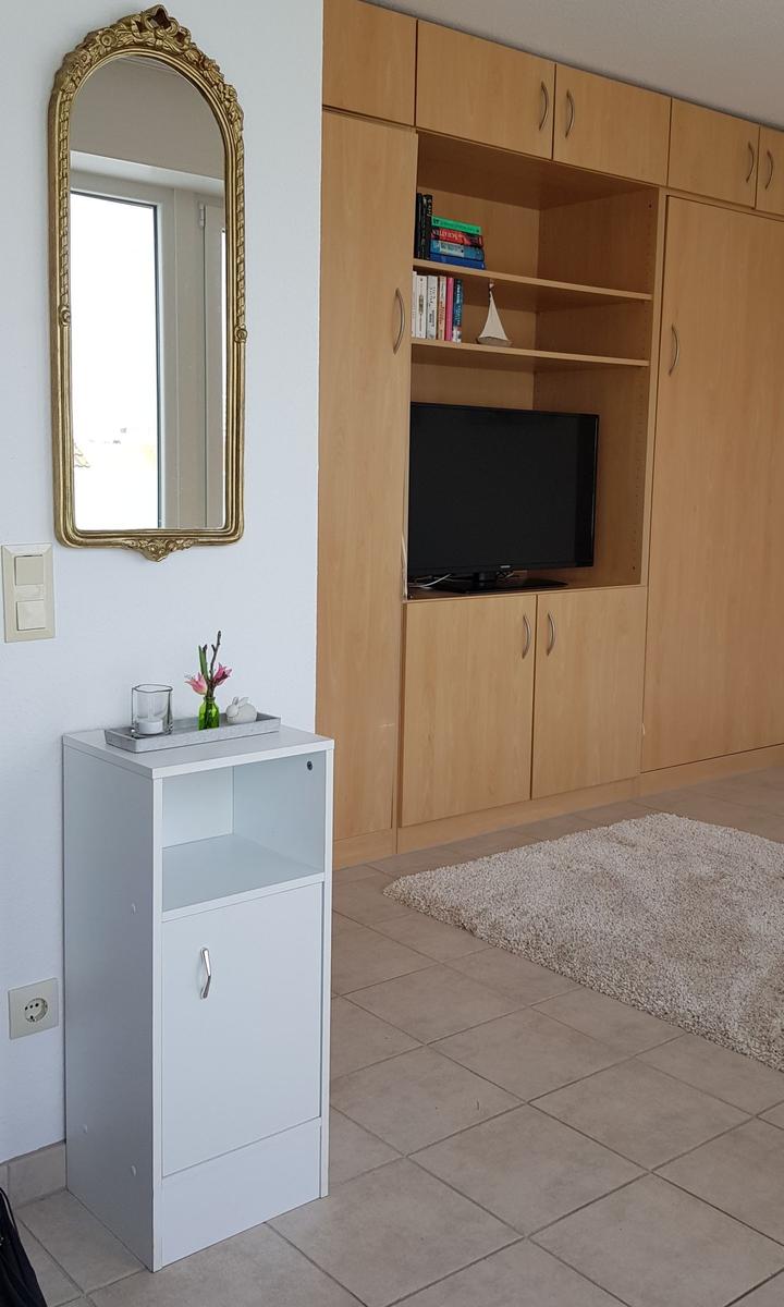 Ein Raum mit Holzschrank, Fernseher, Spiegel und kleinem Schrank.