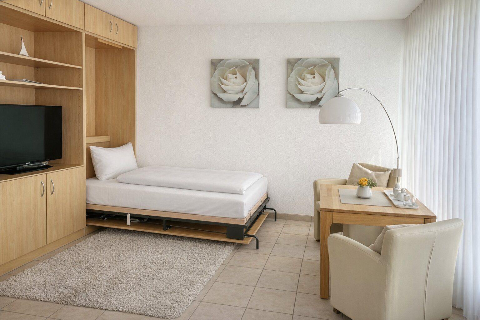 Schlafzimmer mit Bett, TV und Esstisch. An der Wand hängen zwei Bilder.