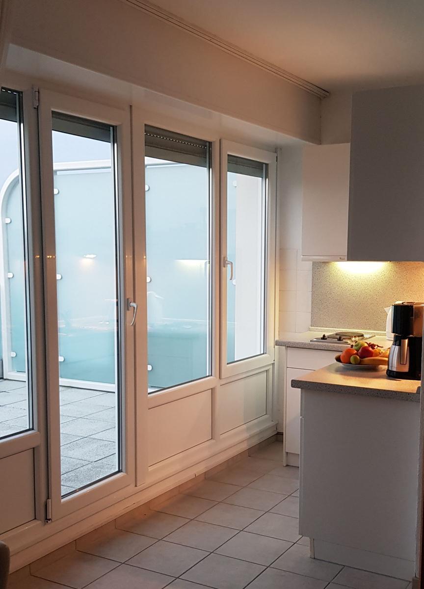 Küche mit Blick auf Balkon. Weiße Schränke und Fliesenboden.