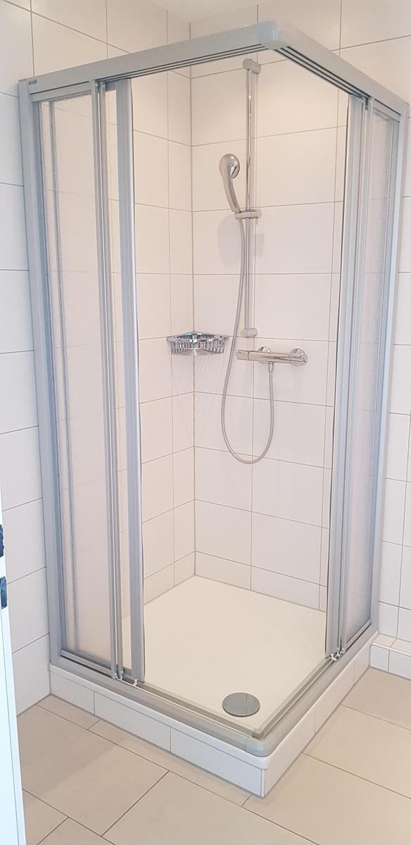 Duschbereich mit Duschkabine, Handbrause und Duschschaumhalter.