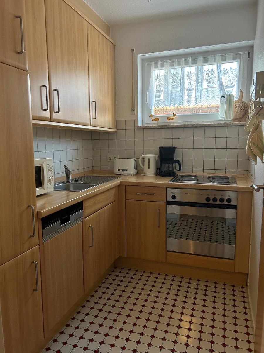 Küche mit Holzschränken, Spüle, Herd und Fenster mit Vorhängen.