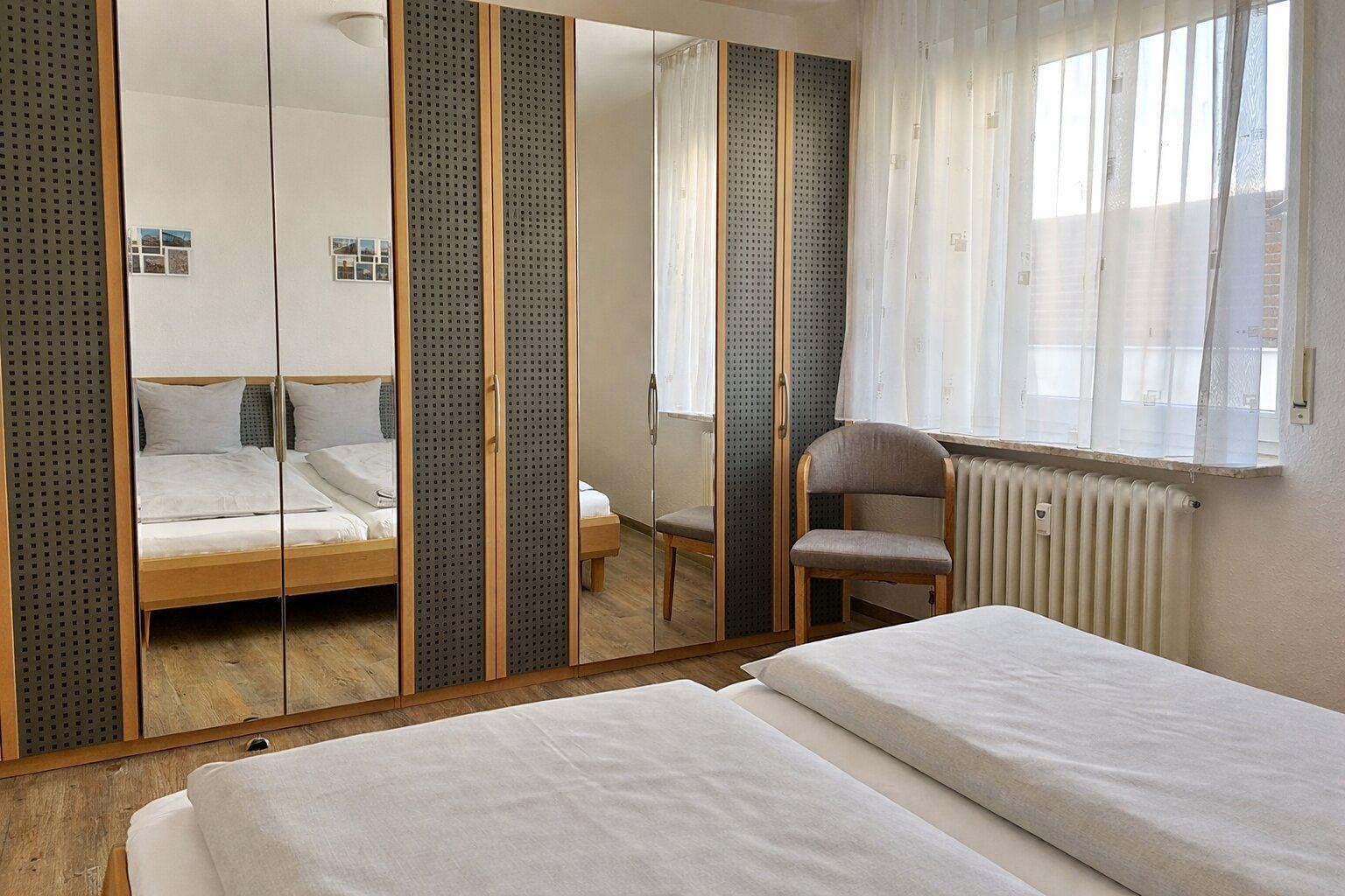 Zimmer mit Doppelbett, Spiegelschrank und Fenster mit Vorhängen.