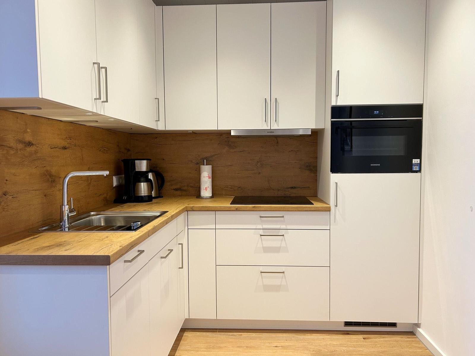 Moderne Küche mit weißen Schränken, Holz Arbeitsplatte und integriertem Herd.