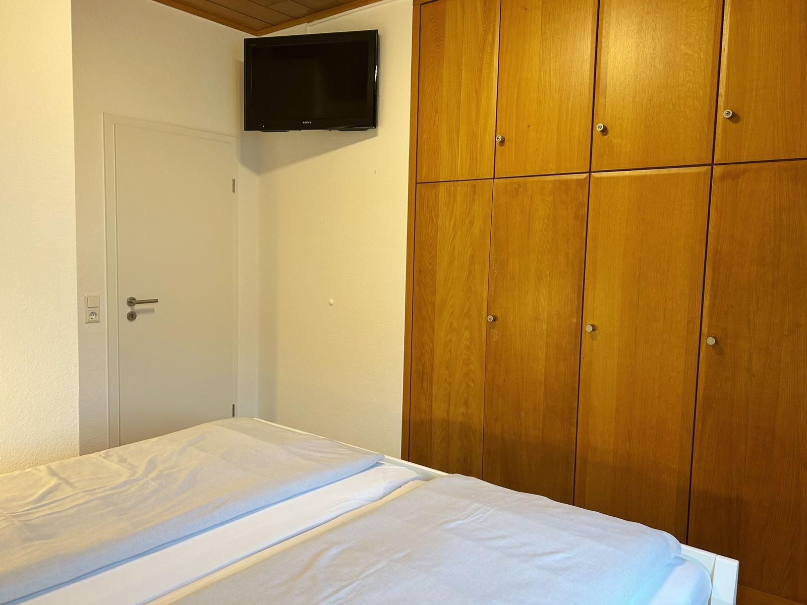 Schlafzimmer mit Bett, Holzschrank und Wandfernseher.