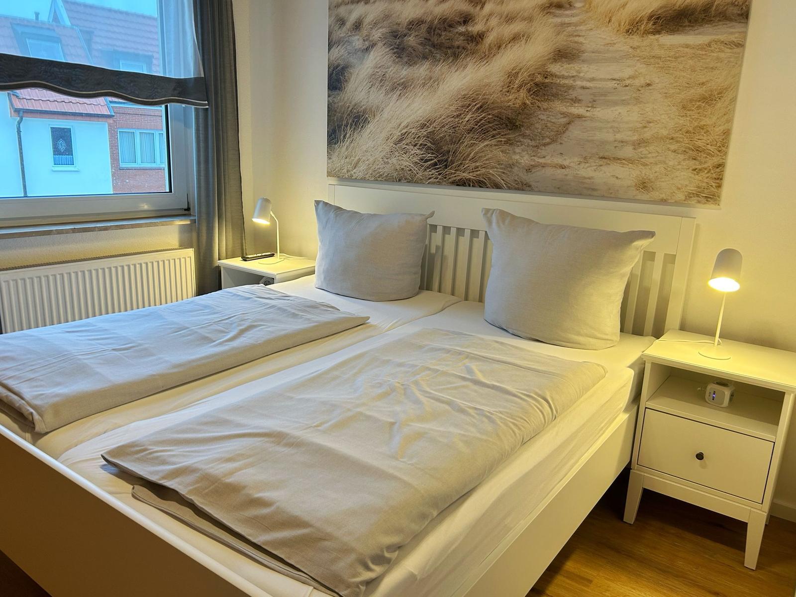Ein Schlafzimmer mit Doppelbett, zwei Nachttischen und einem Fenster mit Blick auf Gebäude.