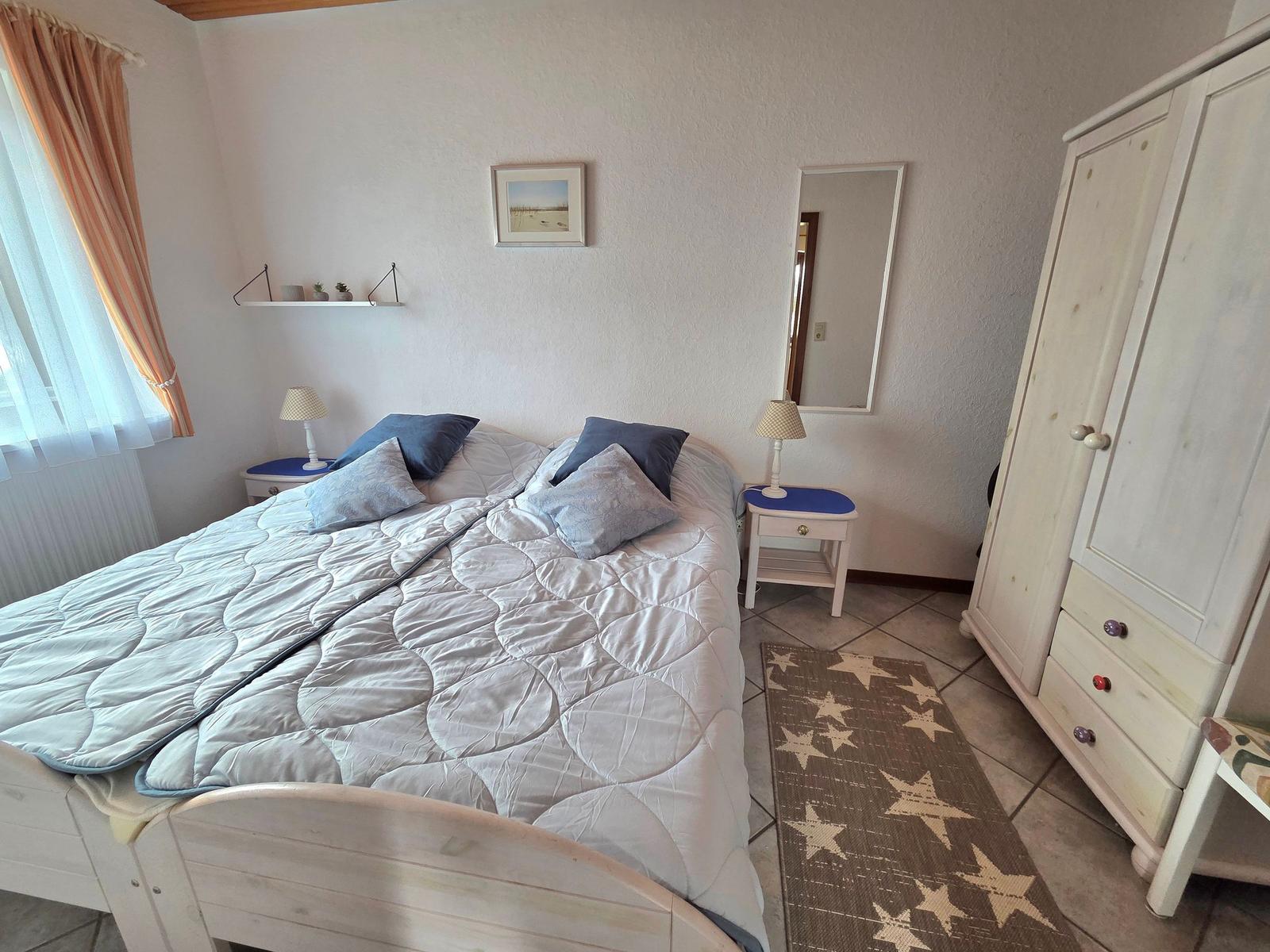 Schlafzimmer mit Bett, Nachttischen, Kleiderschrank und Fenster mit Vorhängen.