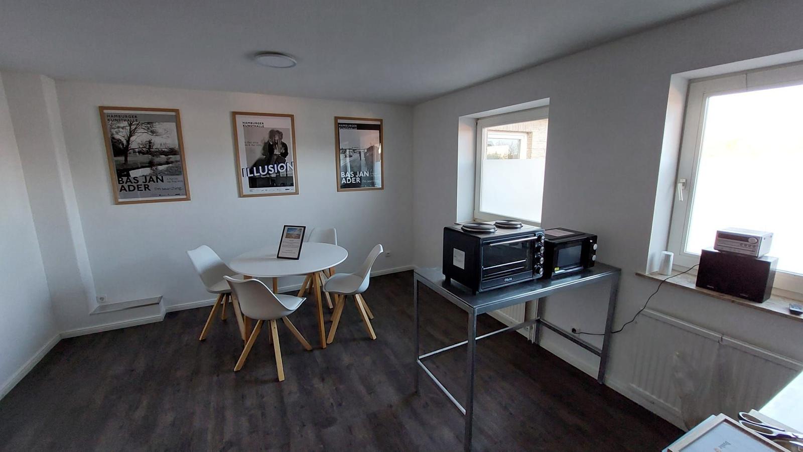Essbereich mit Tisch, Stühlen und drei Wandplakaten. Küchenzeile mit Toaster und Mikrowelle.