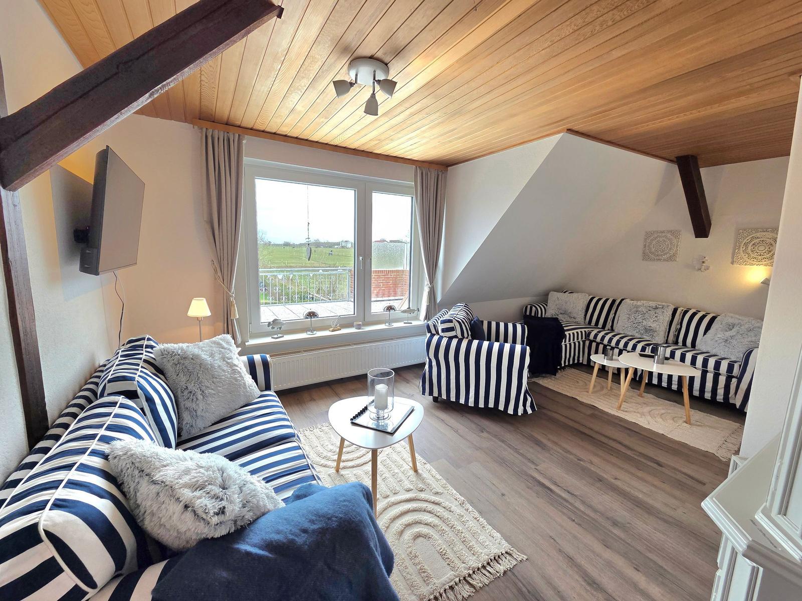 Wohnzimmer mit Holzdecke, Sofa und Sessel mit Streifen, Fenster mit Blick auf Balkon.