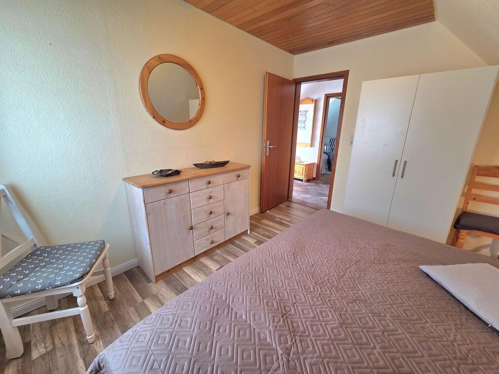 Schlafzimmer mit Bett, Kleiderschrank und Schminktisch mit runden Spiegel.