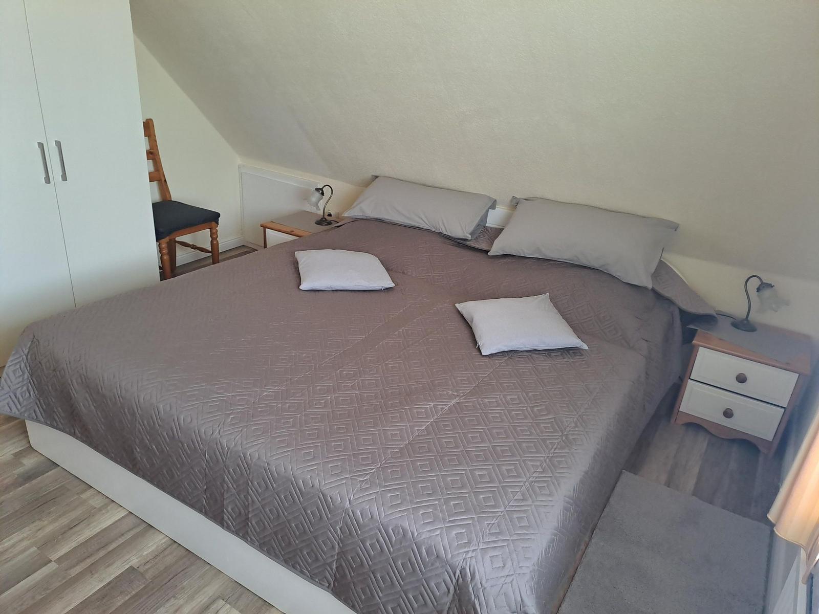 Schlafzimmer mit Doppelbett, Nachttischen und Stuhl unter schräger Decke.