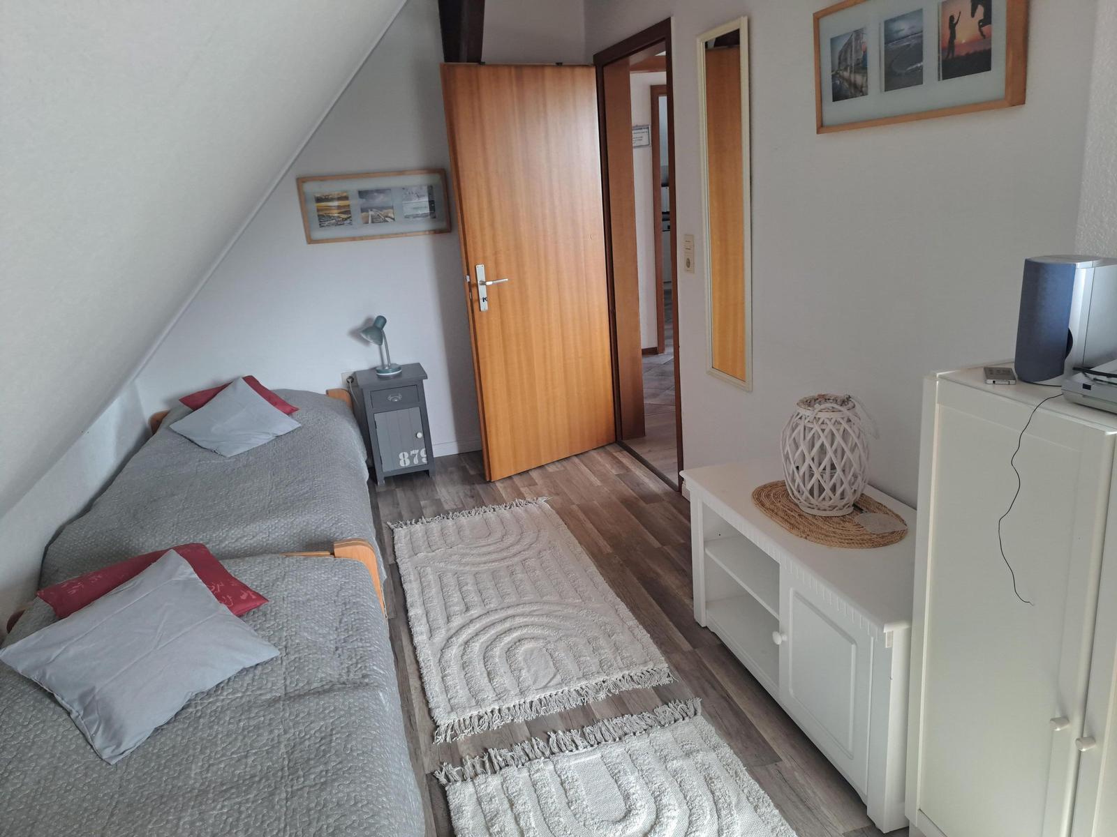 Schlafzimmer mit Dachschräge, Bett, Kleiderschrank und Teppich auf Holzboden.
