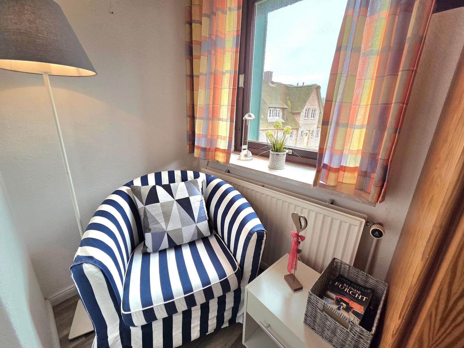Ein Sessel mit Streifenmuster steht vor einem Fenster mit bunten Vorhängen.
