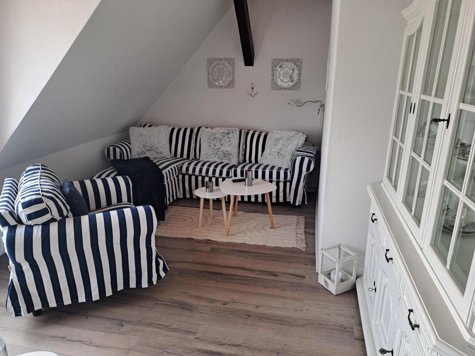 Wohnzimmer mit schwarz-weiß gestreifter Couch, Holzboden und weißem Schrank.