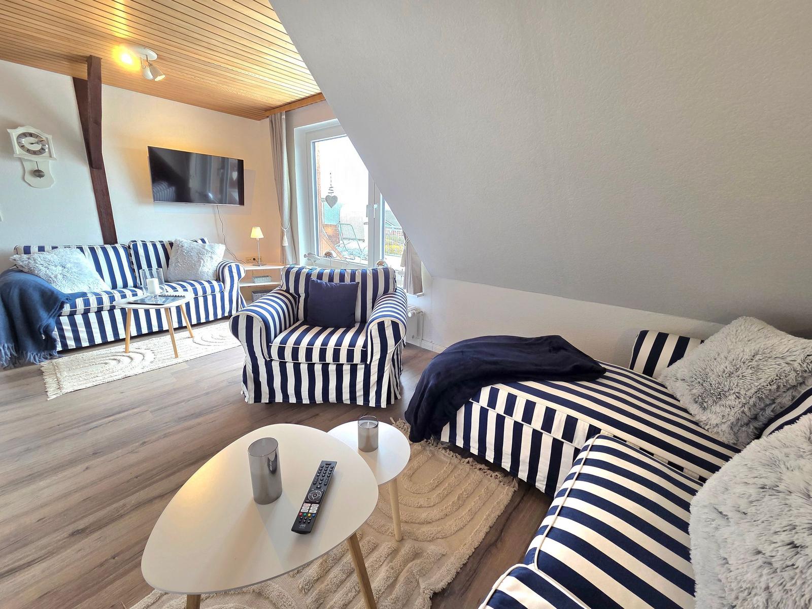 Wohnzimmer mit gestreiften Sofas, Fernseher und Fenster zum Balkon.