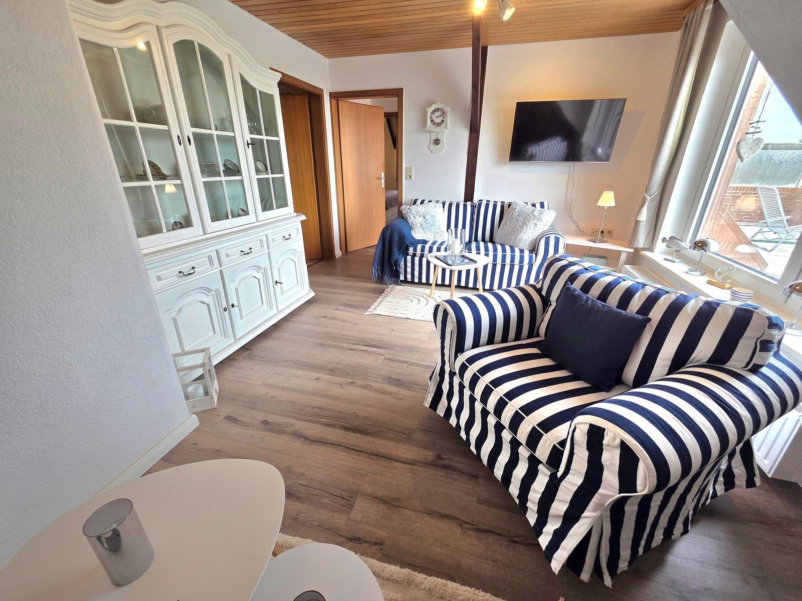 Wohnzimmer mit gestreiftem Sofa, weißen Schränken und Fernseher an der Wand.