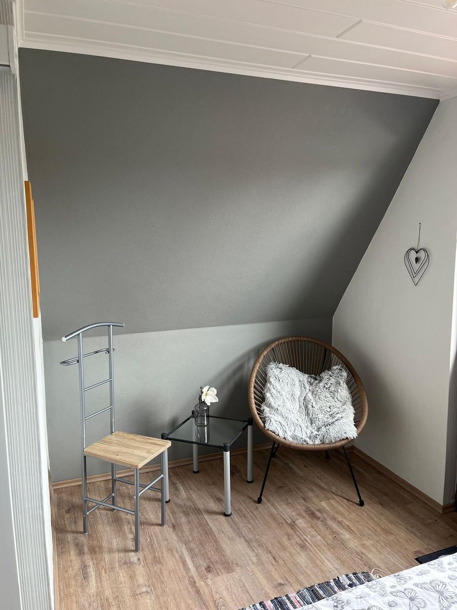 Schlafzimmer mit Sessel, Tisch und Stuhl unter Dachschrägen.