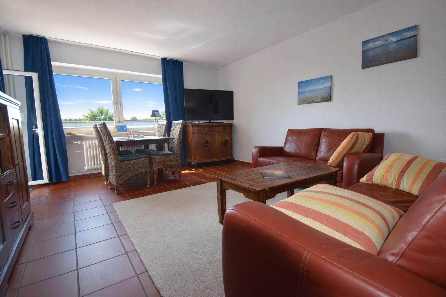 Wohnzimmer mit Sofa, Esstisch und TV. Blick auf Wasser durch Fenster.