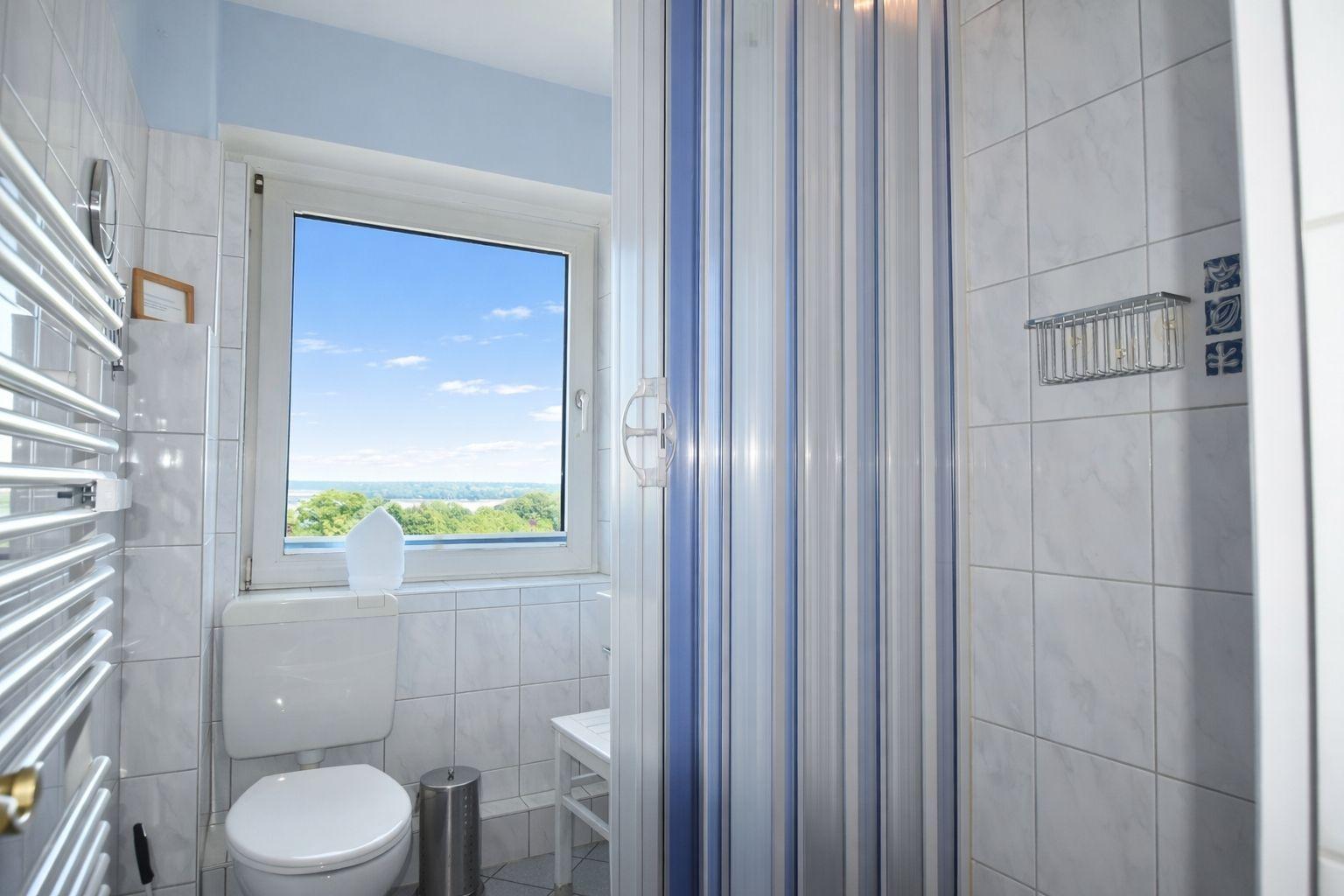 Badezimmer mit Dusche, Toilette und Fenster mit Blick auf Landschaft.