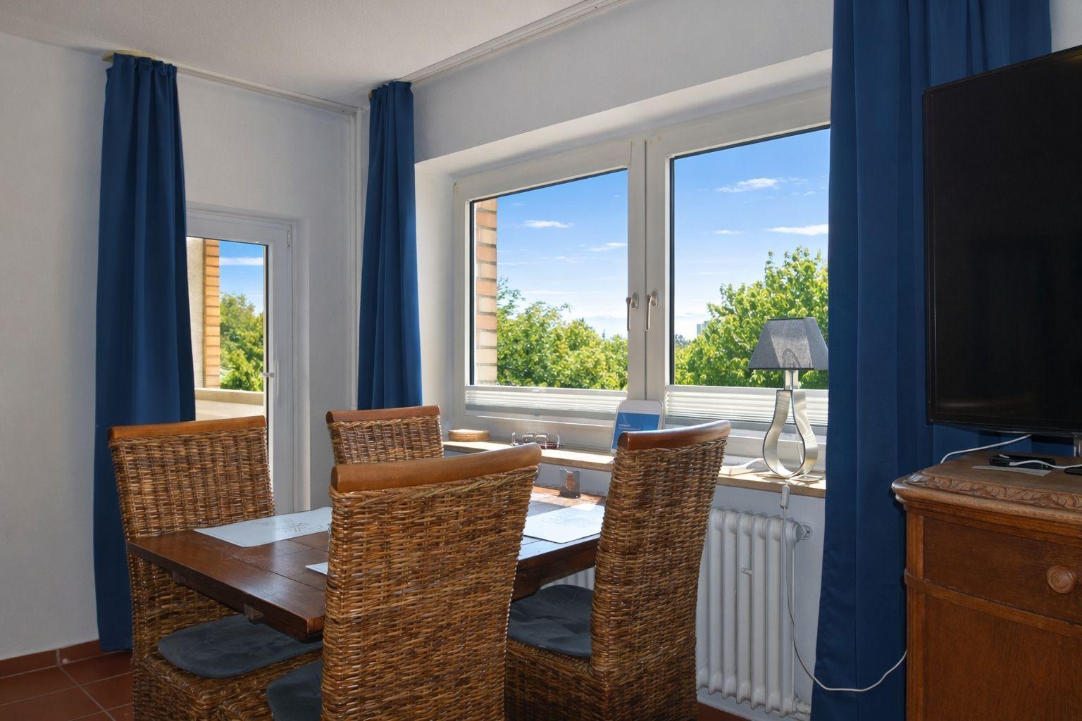 Esszimmer mit Tisch, Stühlen und Fensterblick auf Grün.