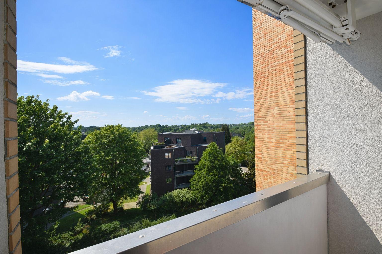Balkon mit Blick auf grüne Bäume und ein modernes Gebäude unter blauem Himmel.