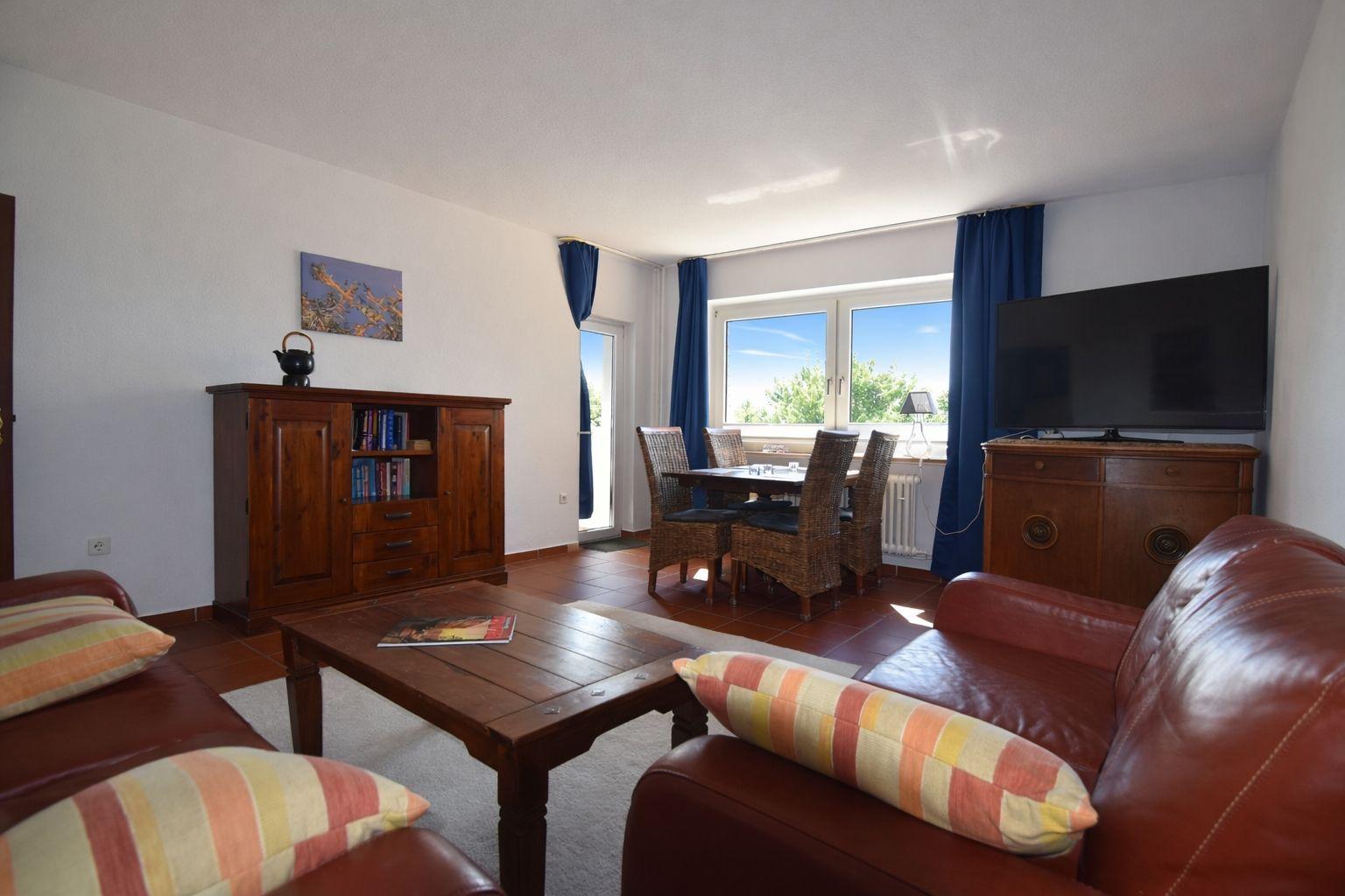 Wohn- und Essbereich mit Sofa, Esstisch und TV. Fenster mit Blick auf Grün.