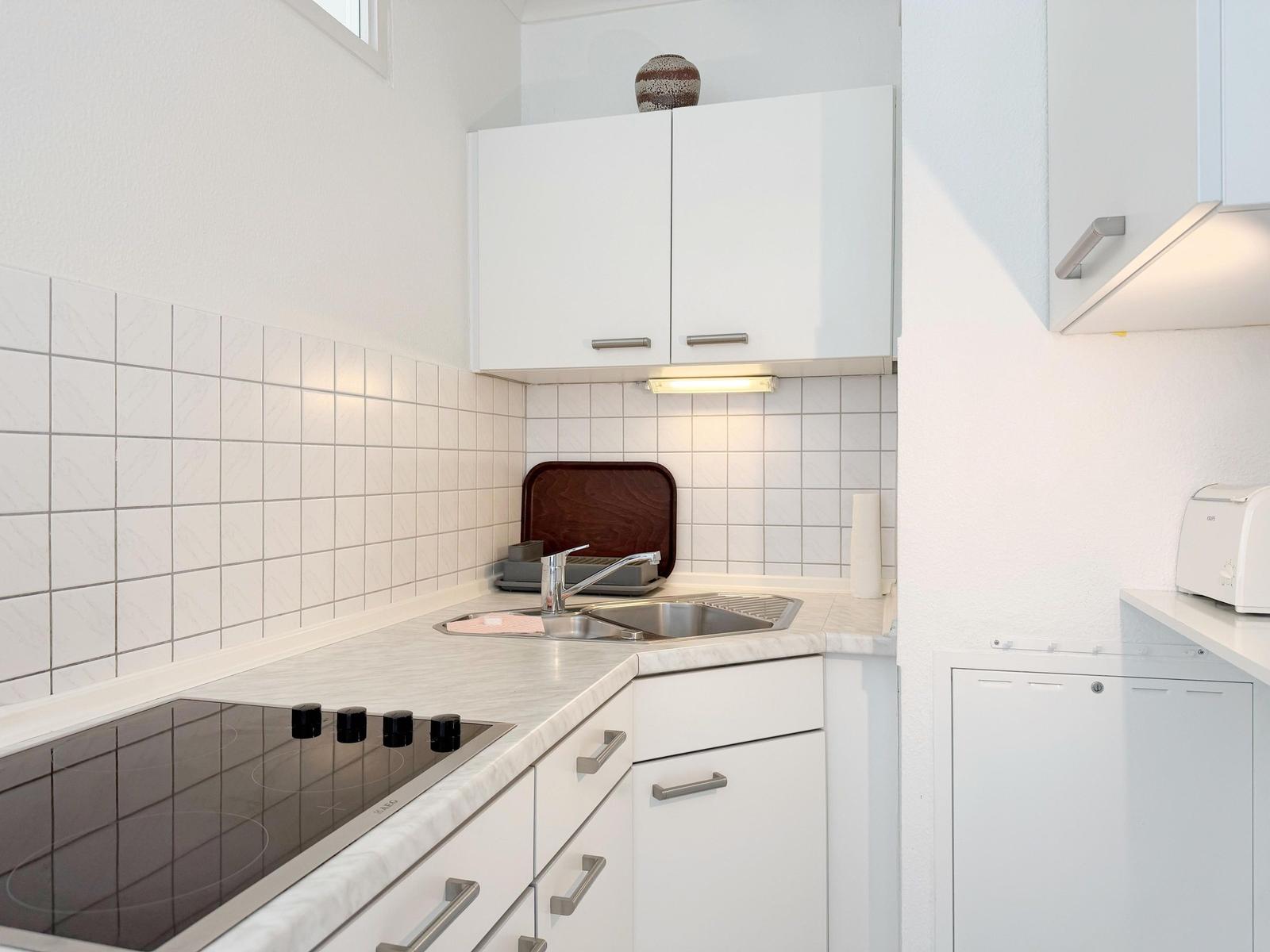 Küche mit weißen Schränken, Edelstahlspüle und Induktionskochfeld.