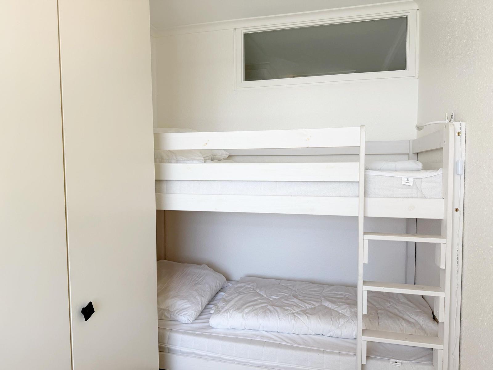 Zimmer mit weißem Doppelstockbett und Fenster über dem oberen Bett.
