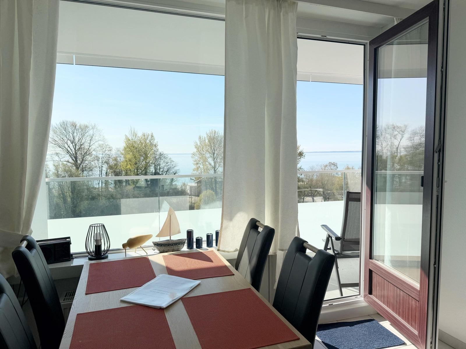 Esstisch mit roten Untersetzer und Aussicht auf Wasser und Bäume.
