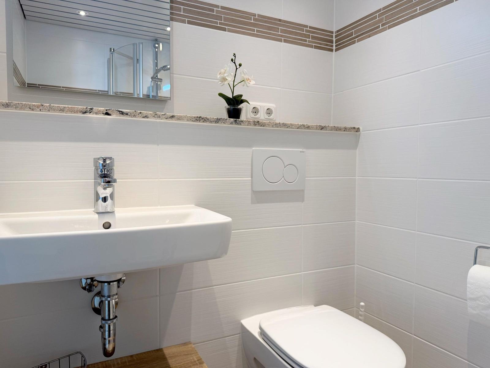 Badezimmer mit Waschbecken, Spiegel, Toilette und Pflanze.